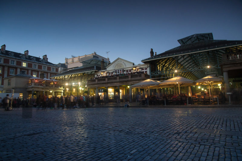 Covent Garden in London at Dusk with a crowd gathering to the left to watch the street performers.